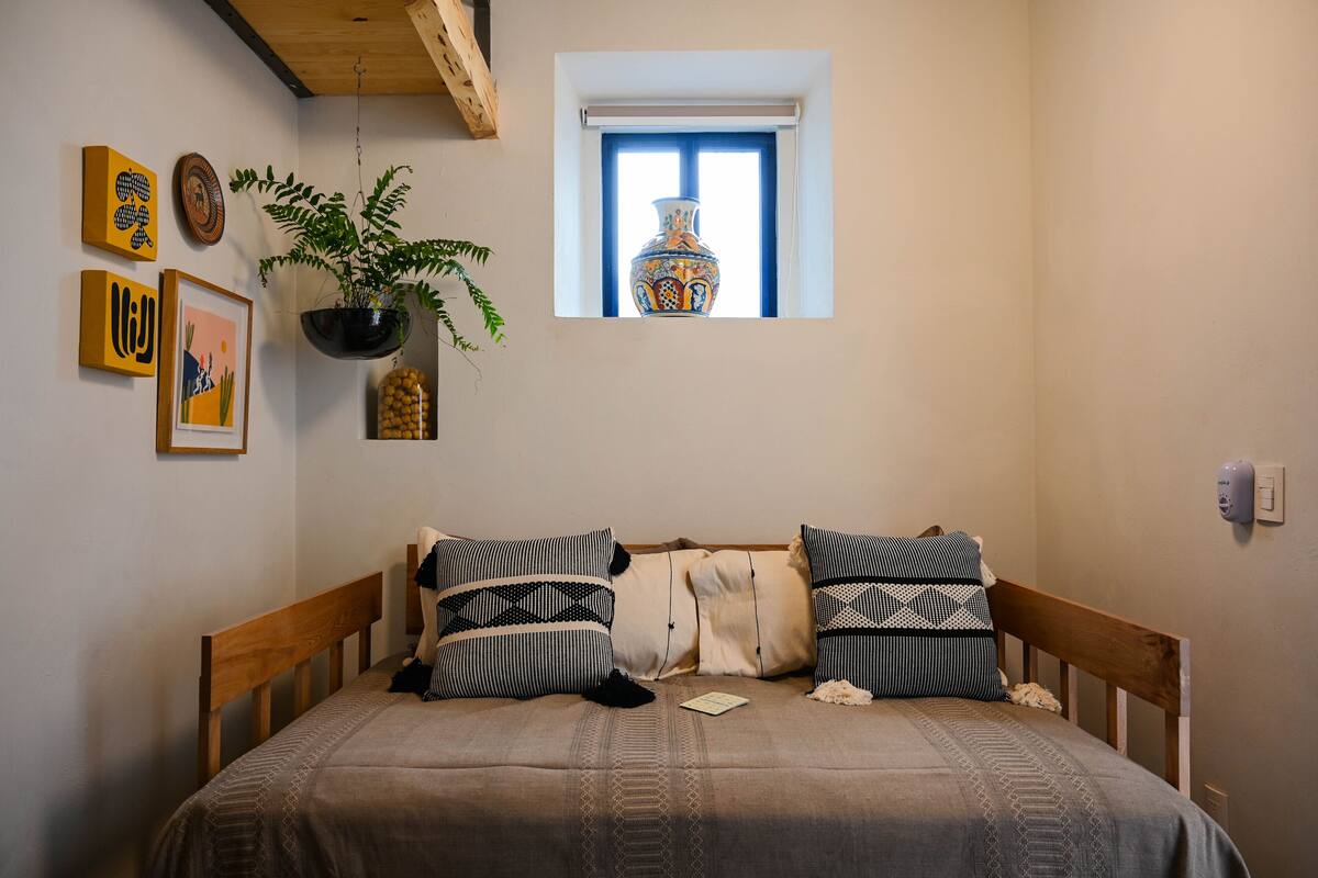 Une chambre à coucher avec un lit, une fenêtre agrémentée d’un vase et des décorations murales.