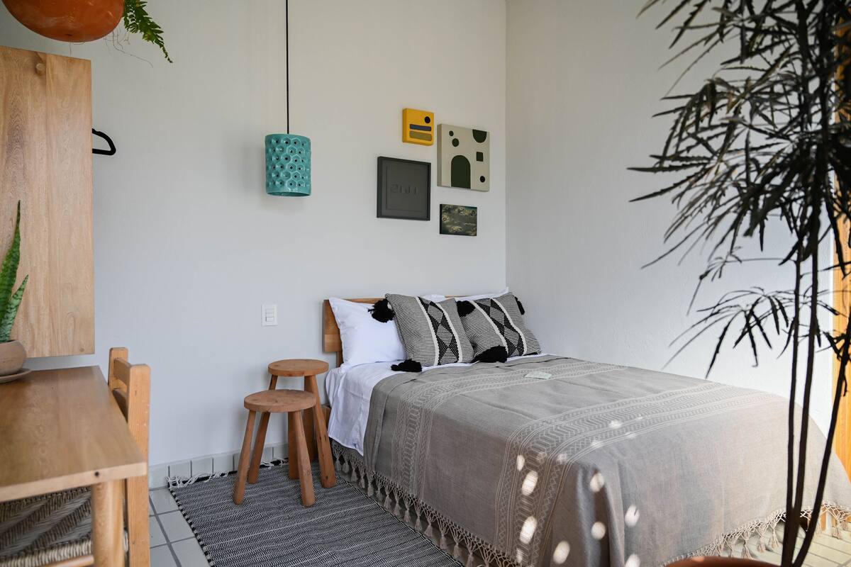 Une chambre à coucher comprenant un lit, une table de chevet en bois, un luminaire suspendu et une étagère fixée au mur.