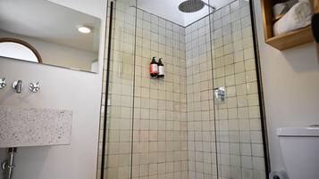 Un baño en esquina con ducha, inodoro, lavabo y espejo.