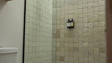 A bathroom with a toilet, a shower with a glass door, and a shelf with folded towels.