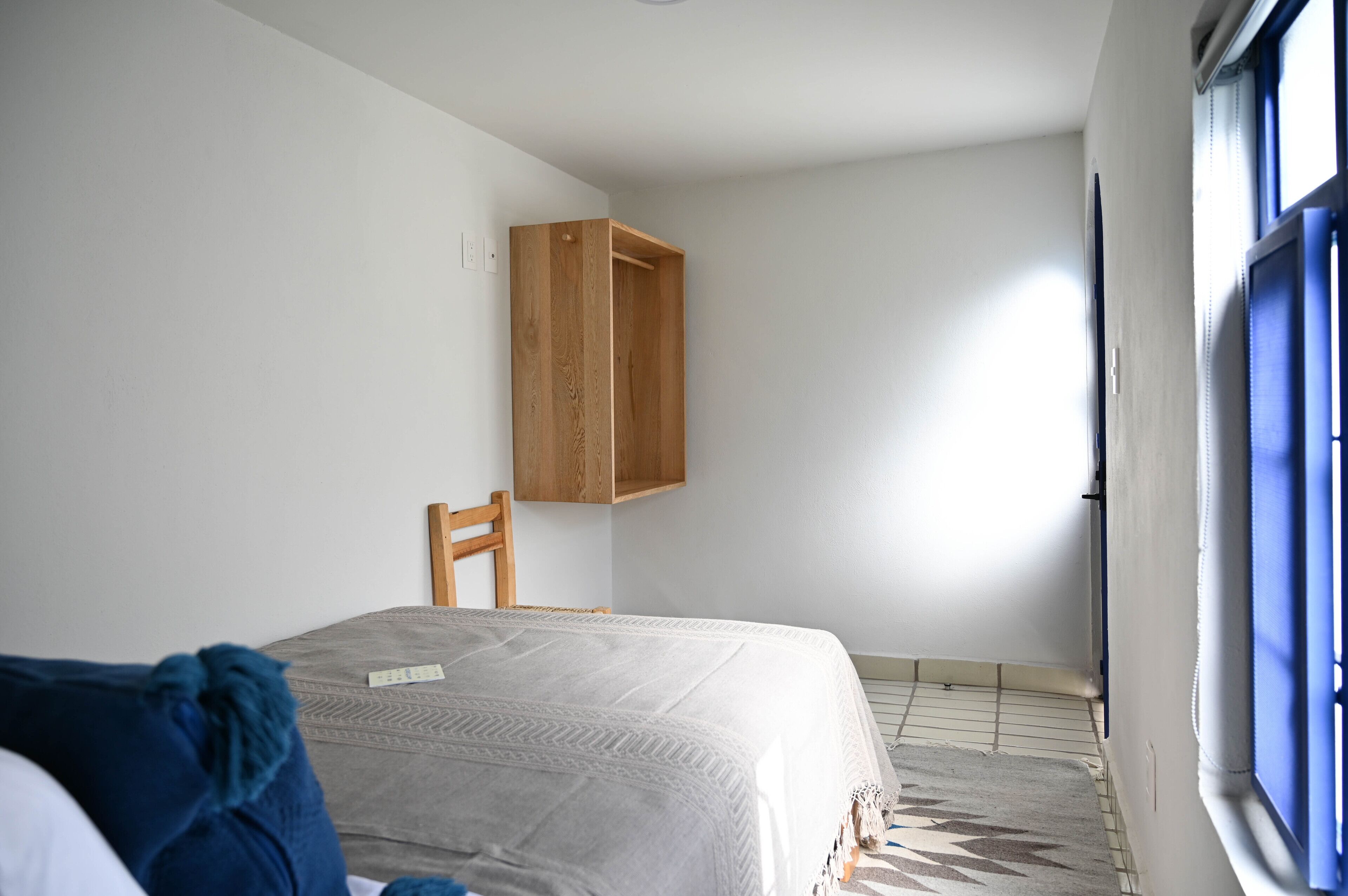 Ein Schlafzimmer mit einem Bett, einem Holzschrank, einem Sessel und einem Fenster mit blauen Jalousien.