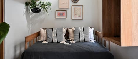 Quarto com cama de madeira, planta pendente e quadros nas paredes.