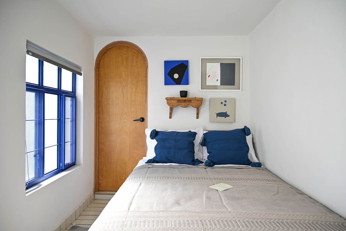 Une chambre à coucher avec un lit, une porte en bois, une fenêtre et des œuvres d’art murales.