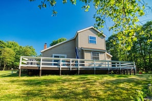A two-story house with a deck, surrounded by lush greenery. - Modern Forest Retreat w/ Private Hot Tub, Fire Pit & Deck! (Albrightsville)