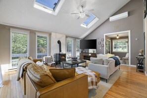 Ein großzügiger Wohnraum mit Kamin, Deckenventilator und großen Fenstern.