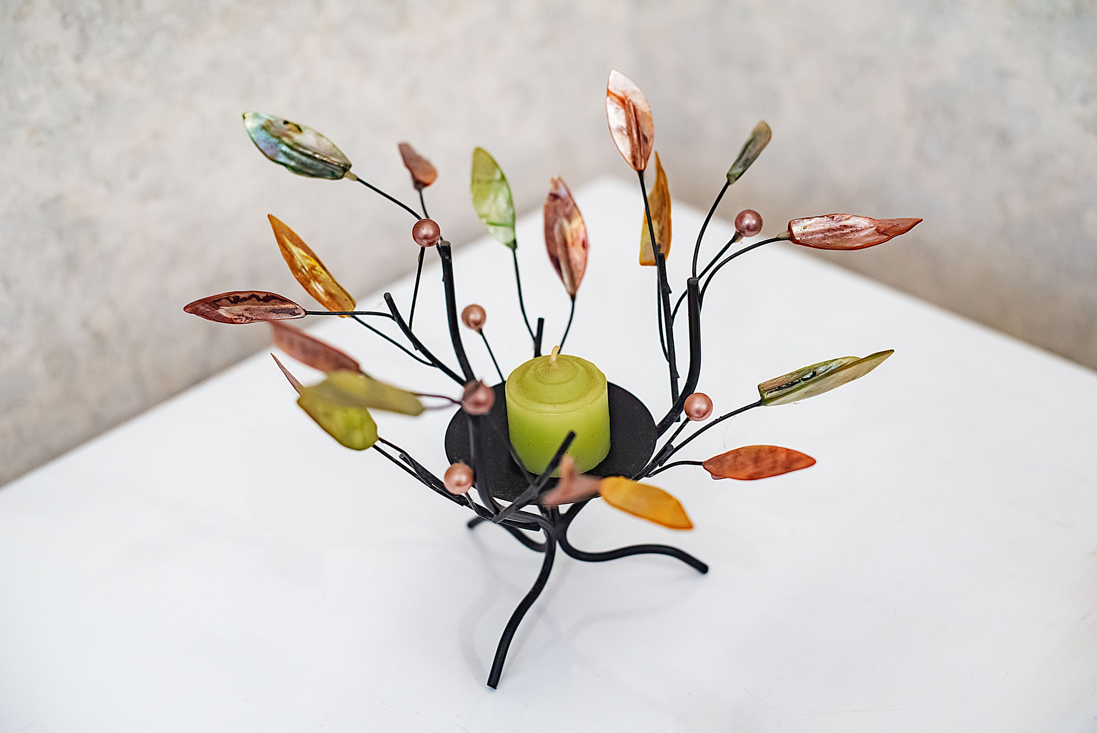 A decorative centerpiece with a green cylindrical base and branches adorned with leaves and beads.