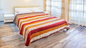 A bedroom with a wooden floor, a bed with a striped quilt, a bedside table, and a wall-mounted light. - H&B apartments Ierusalim (Tbilisi)