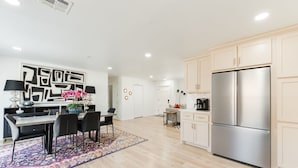 A modern kitchen with light wooden cabinets, a stainless steel refrigerator, and a dining area with a black and white table set. - Beautifully Remodeled-Newly Furnished-Cozy, Colorful & Eclectic Home in N OKC!  (Oklahoma City)