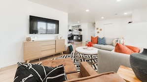 A modern living room with a sofa, coffee table, and a TV mounted on the wall. - Beautifully Remodeled-Newly Furnished-Cozy, Colorful & Eclectic Home in N OKC!  (Oklahoma City)