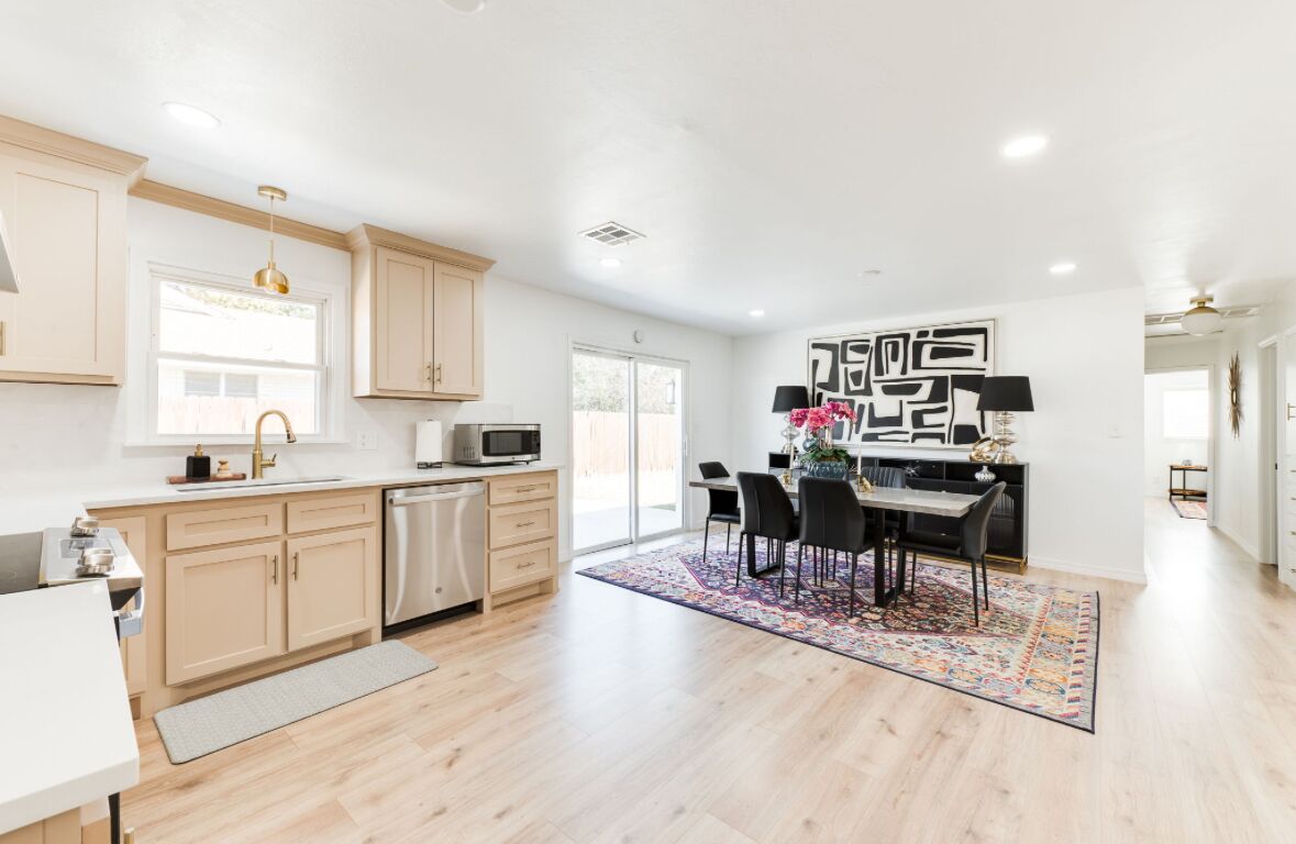 A modern kitchen with light wood cabinets, a dishwasher, and a dining area with a black table and chairs.