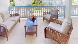 A covered outdoor seating area with wicker furniture and a table, overlooking a residential neighborhood.