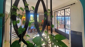Une pièce offrant une vue à travers un paravent décoratif, un balcon avec une grille en métal, et un aperçu d’un coin repas avec une table et des chaises.