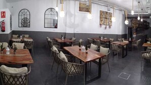 A restaurant interior with multiple wooden tables and wicker chairs, a fire extinguisher on the wall, and decorative wall art. - Hotel Lua Isla Del Hierro (El Pinar de El Hierro)