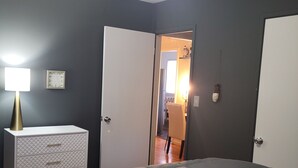 Un dormitorio con cama, cómoda, lámpara y una puerta que da a otra habitación.