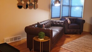 Una sala de estar con un sofá modular, una mesita auxiliar, un adorno de pared y una ventana con persianas.