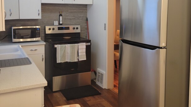 Una cocina compacta con armarios blancos, un refrigerador de acero inoxidable, un microondas y un horno.