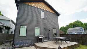 Et toetagers hus med en patio, grill, udendørs møbler og en lille træterrasse.