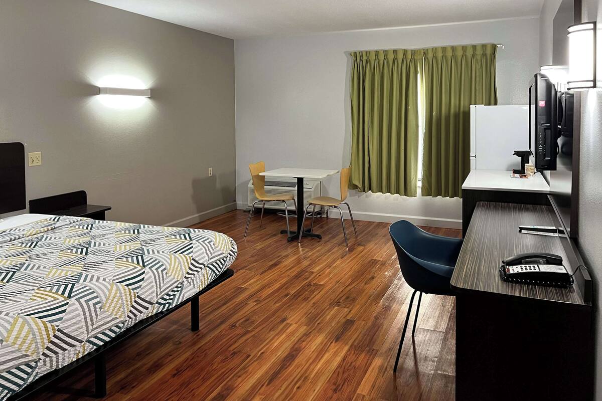 A hotel room with a bed, a desk with a telephone, a chair, a small table, and a window with curtains.