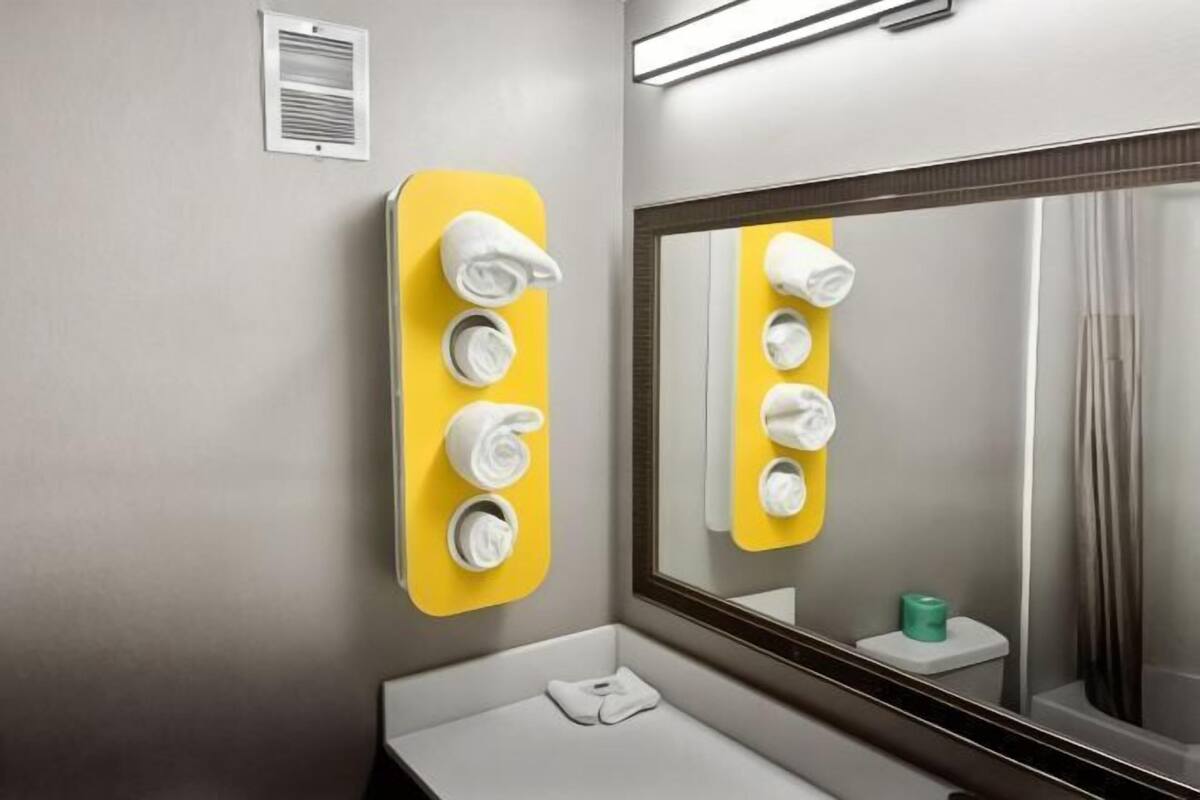 A bathroom with a mirror, a yellow towel rack, a white sink, and a toilet.