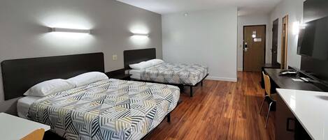 A hotel room with two beds, a desk, a TV, and a door leading to a bathroom.