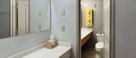 Une salle de bain avec un lavabo blanc, un miroir, un distributeur de serviettes et des toilettes.