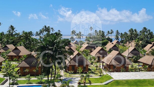 A resort with multiple bungalow-style buildings, a swimming pool, and palm trees.
