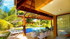 A poolside area with a glass table and chairs, a hammock, and a view of a swimming pool.