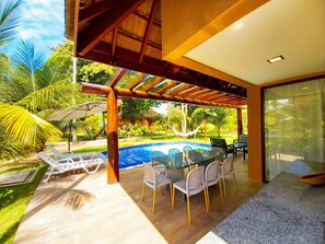 A poolside area with a glass table and chairs, a hammock, and a view of a swimming pool.