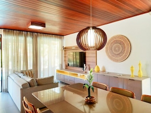 Un salon moderne comprenant un canapé, une table à manger et des chaises. On y trouve également un coin cuisine avec un téléviseur et un élément décoratif mural.