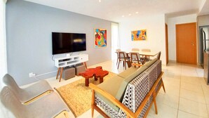 A modern living room with a flat-screen TV, a sofa, a dining table with chairs, and two abstract paintings on the wall.