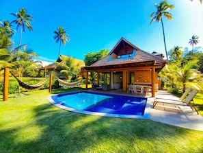 Une maison avec une piscine, un hamac et une terrasse avec des chaises.
