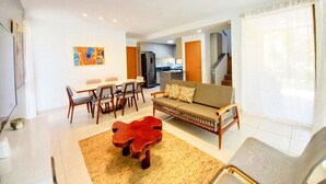 A modern living room with a sofa, dining table, chairs, a coffee table, and a kitchen in the background.