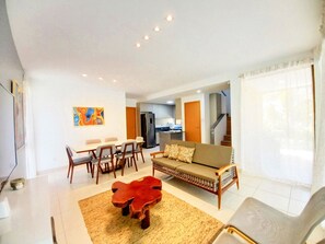 Un salon moderne avec un canapé, une table à manger, des chaises, une table basse et une cuisine en arrière-plan.