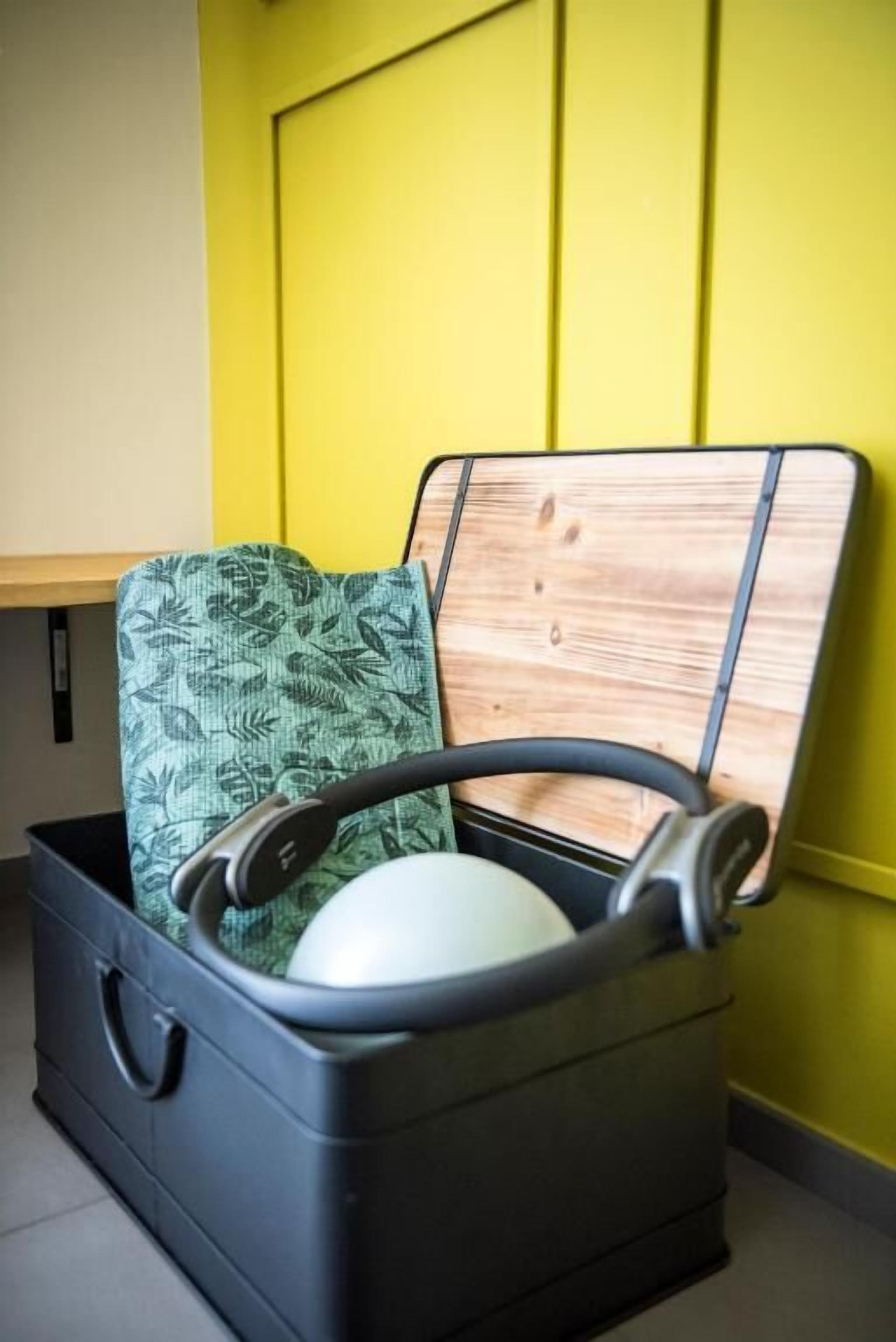 A suitcase with a green patterned pillow and headphones inside, placed on a tiled floor against a yellow wall.