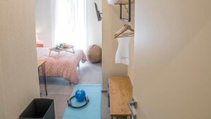 A room with a bed, a desk, a chair, a yoga mat, and a wall-mounted TV.