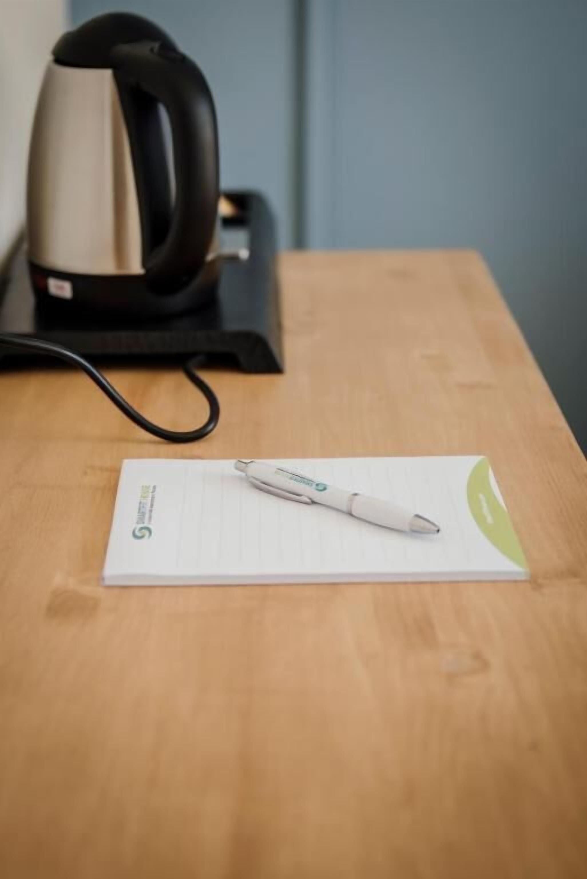 Una tetera, un bolígrafo y una libreta sobre una mesa de madera.