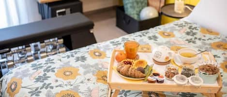 A bed with a floral bedspread, a tray with breakfast items, a bedside table with a lamp, and a bench in the background.