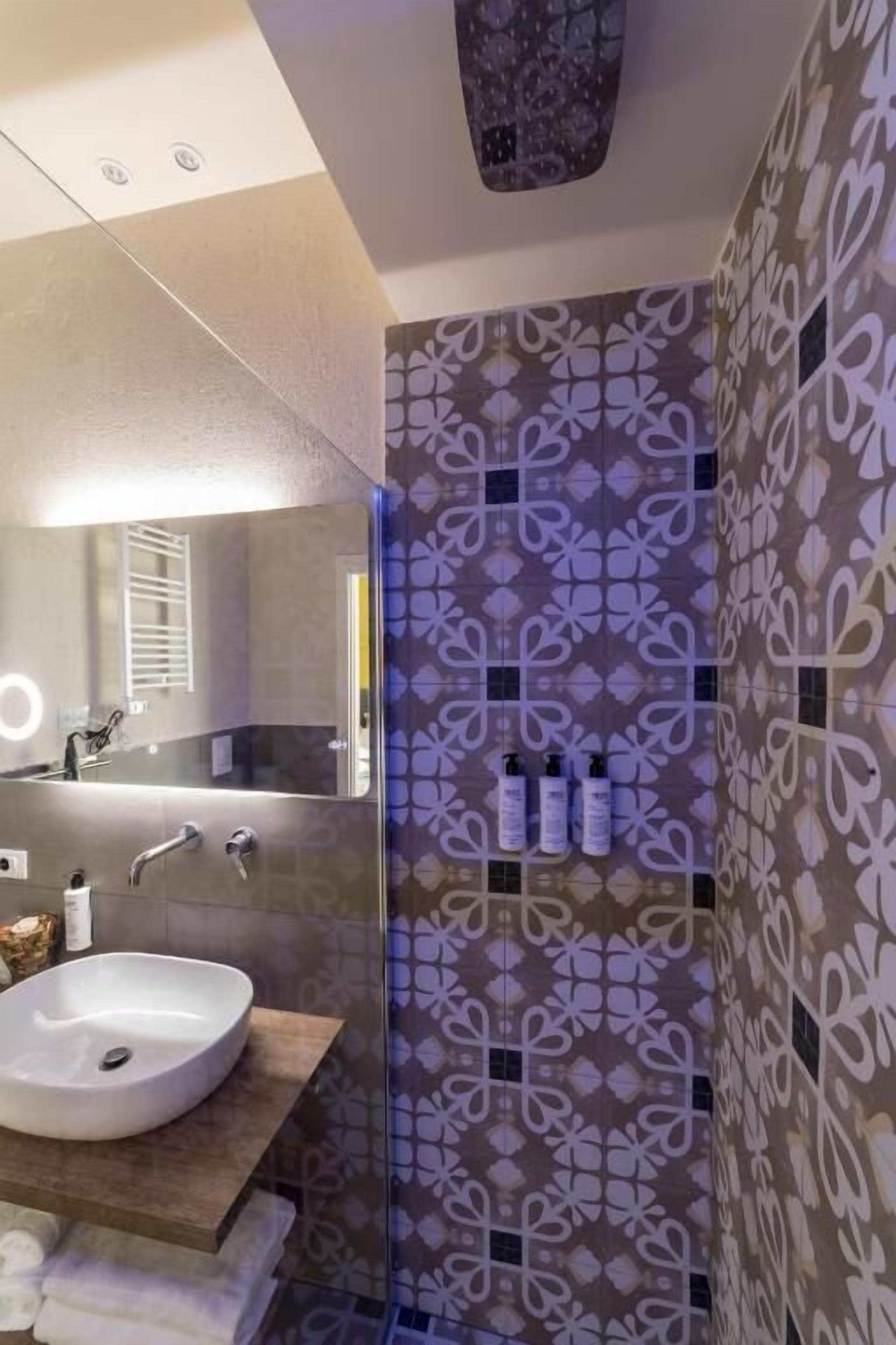 A modern bathroom with a large mirror, a round sink, and a patterned wall.