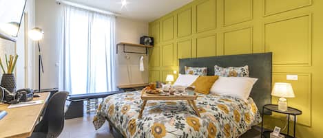 Une chambre à coucher avec une couvre-lit à motifs floraux, une table de chevet avec une lampe et un bureau avec une chaise.