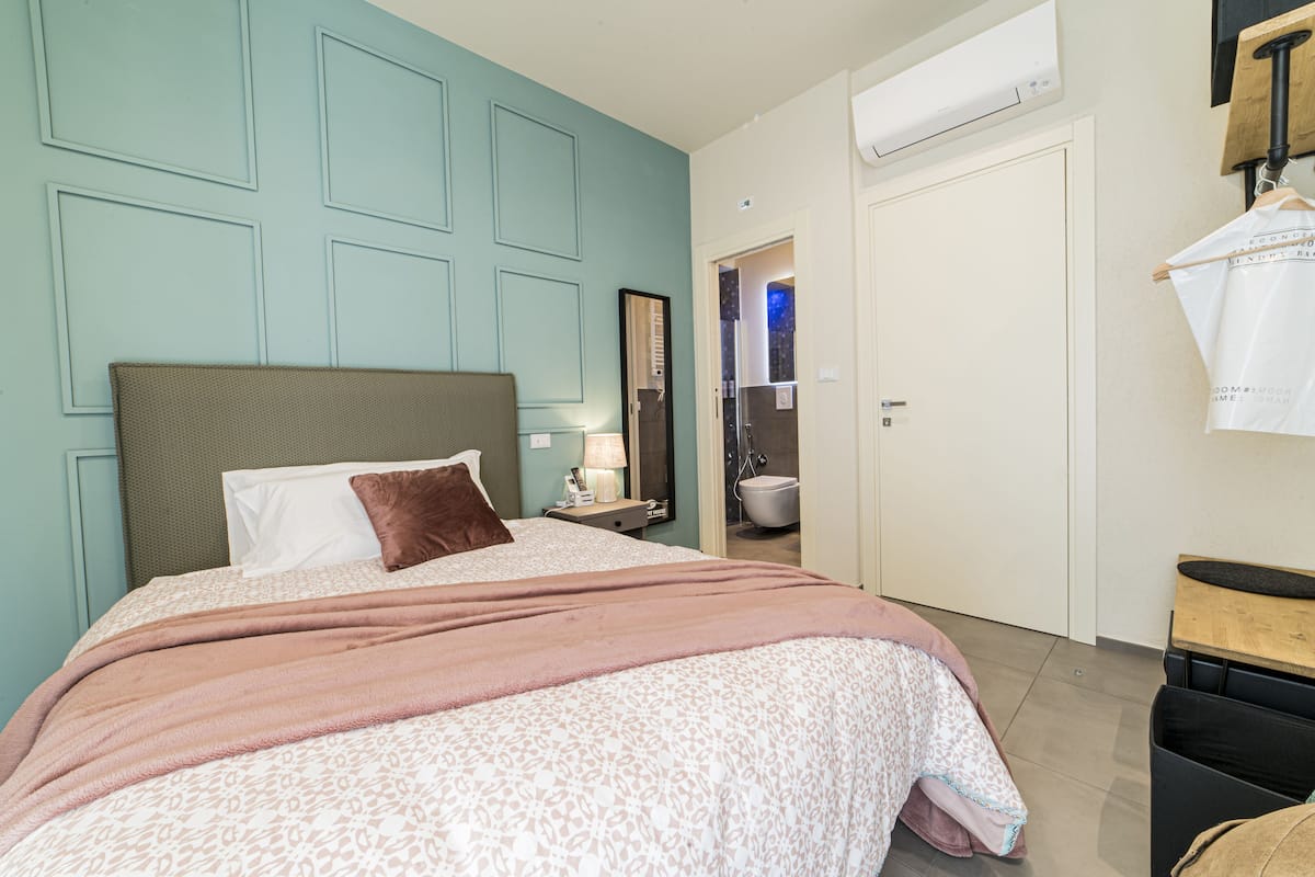 A bedroom with a bed, a nightstand, a lamp, and a bathroom door.