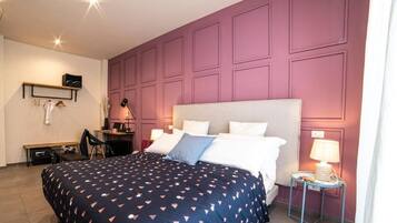 Quarto com uma cama grande, uma escrivaninha e uma cadeira. Há duas mesas de cabeceira com abajures.
