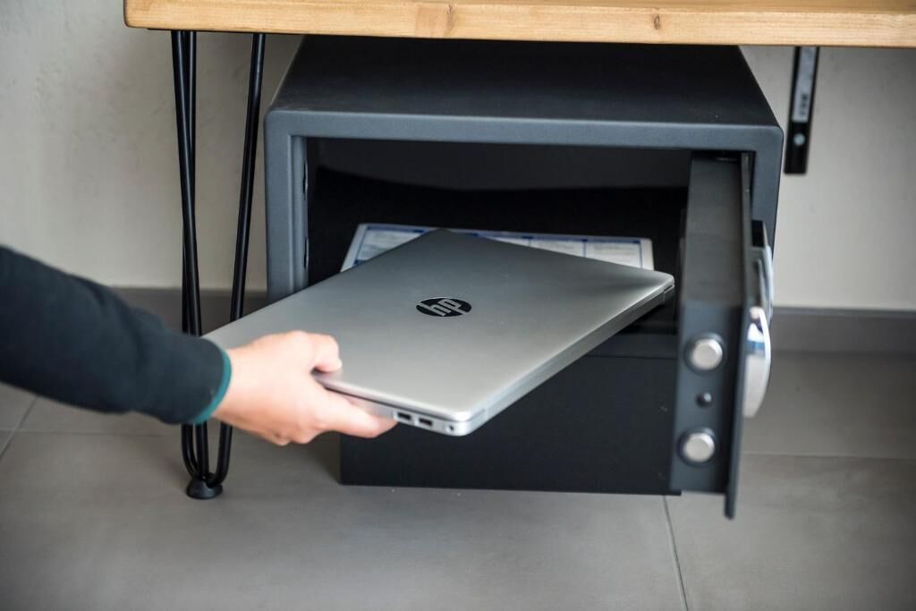 Una persona sosteniendo una computadora portátil cerca de una impresora negra sobre un escritorio.