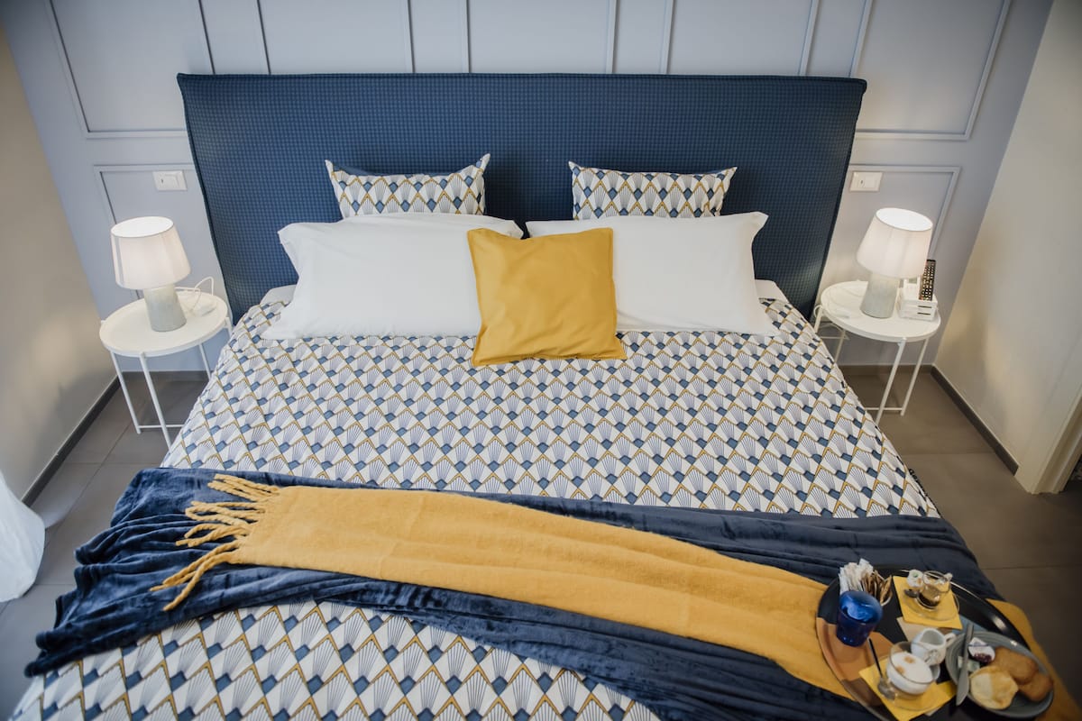 A neatly made bed with patterned bedding, a mustard-colored throw, and a tray with breakfast items.