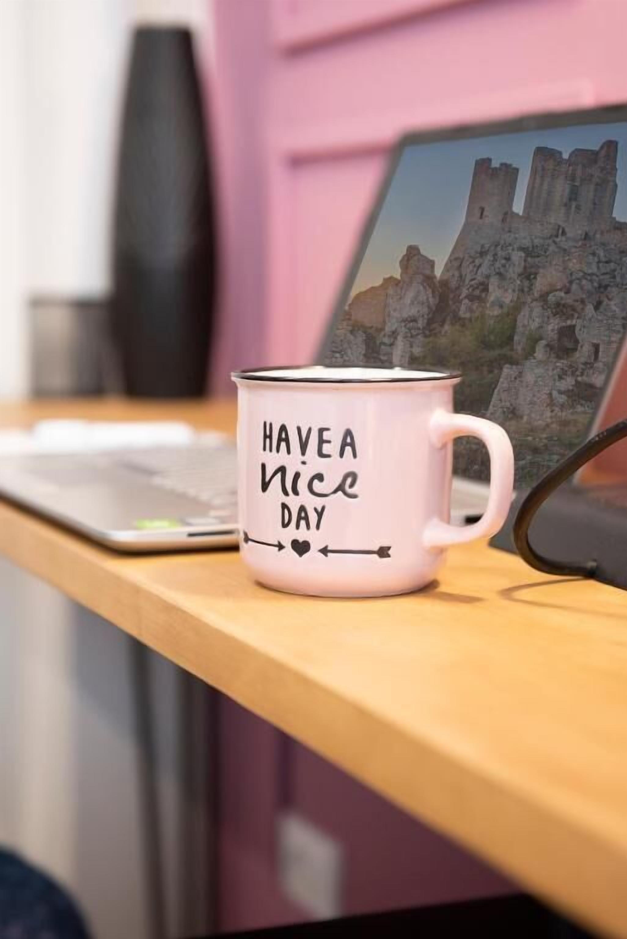 A white mug with "HAVE A NICE DAY" text on a wooden desk.