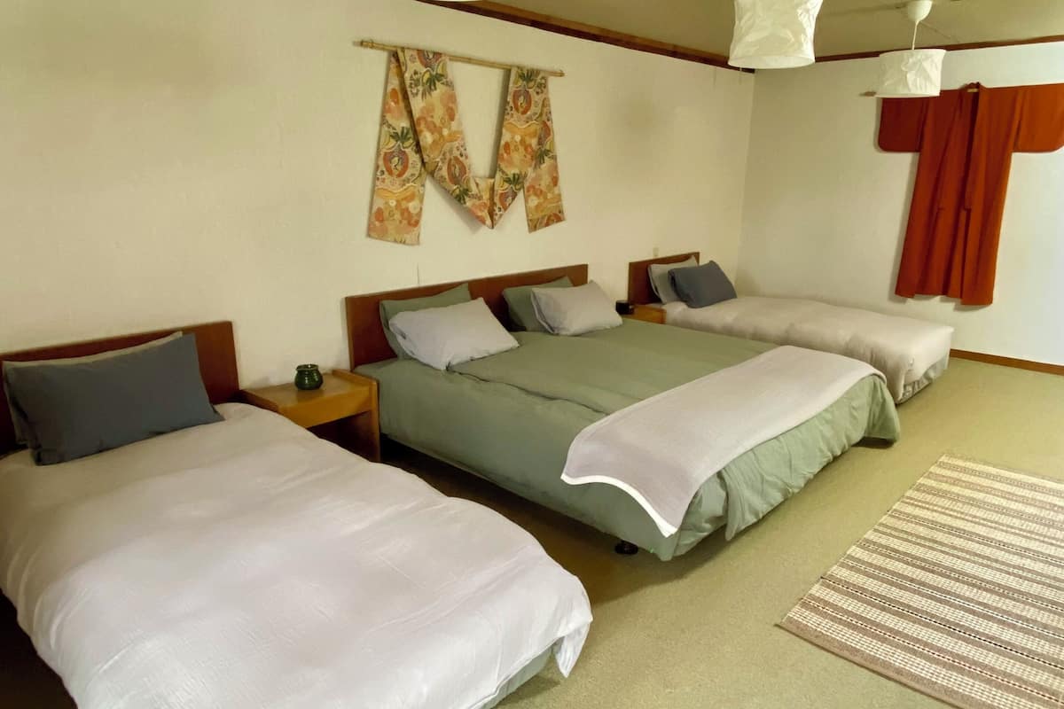 A hotel room with three beds, a hanging light fixture, and a patterned rug.
