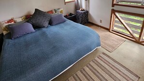 Un dormitorio con una cama grande, un ventilador de techo, un ventanal con cortinas, un cuadro en la pared y vistas al exterior.