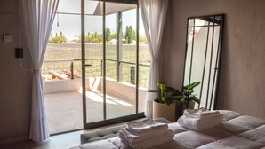 Une chambre d’hôtel dotée d’une grande porte-fenêtre coulissante donnant sur un balcon, d’un lit avec des serviettes soigneusement pliées, d’une plante en pot et d’un miroir au mur.