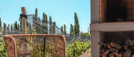 A patio with a table and chairs, a brick oven, and a view of a vineyard.