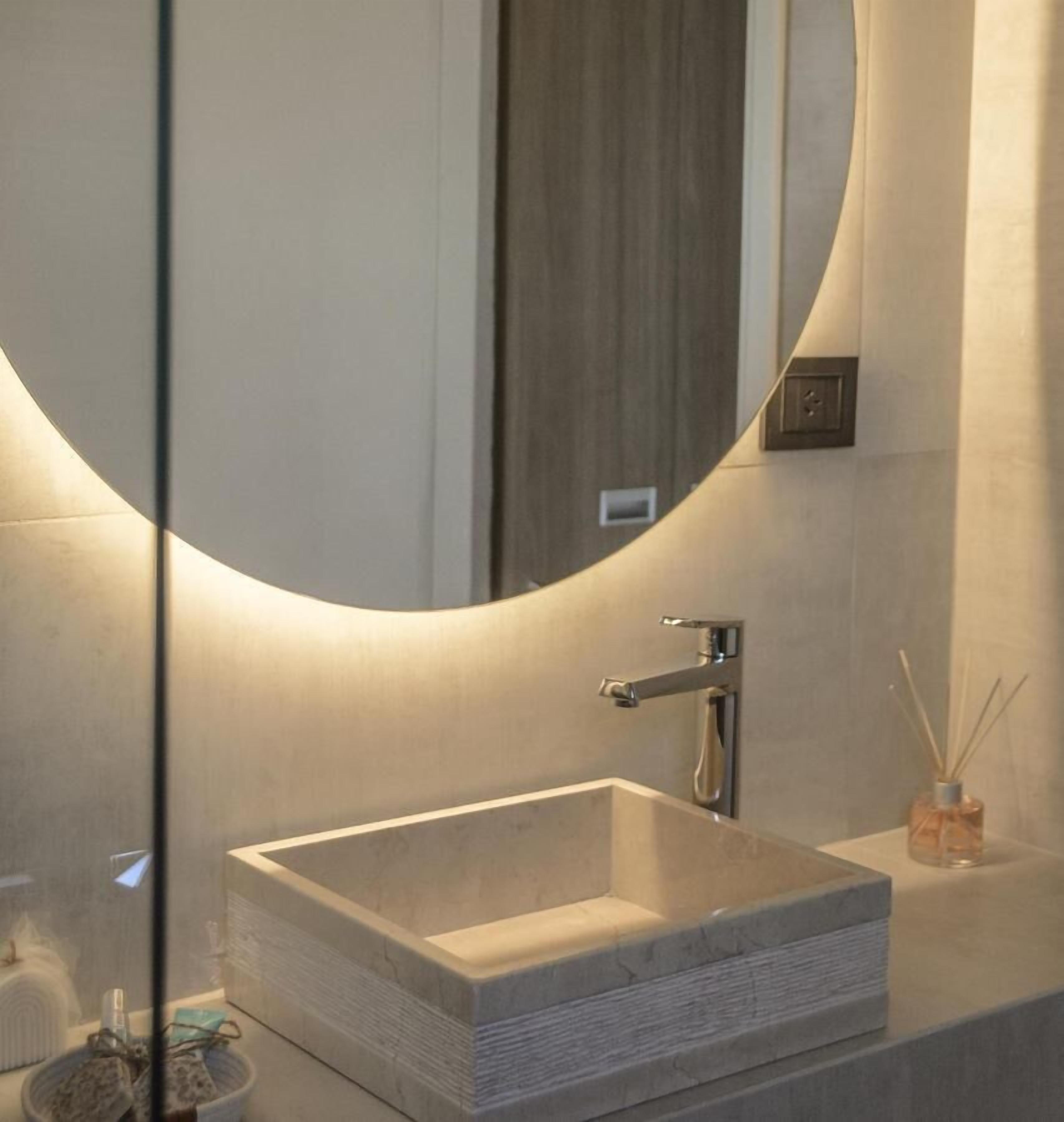 Un baño moderno con un lavamanos de piedra rectangular, un grifo cromado y un espejo redondo con marco de madera.
