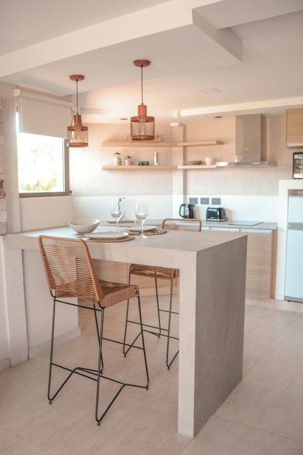 A modern kitchen with a central island, bar stools, pendant lighting, and a view of the outdoors. - Agrelo Vines Lodge (Luján de Cuyo)